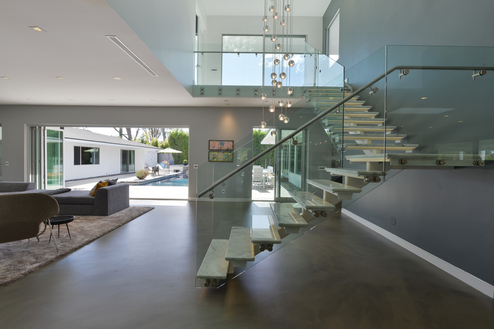 This is an example of a medium sized modern l-shaped glass railing staircase in Los Angeles with open risers and marble treads.