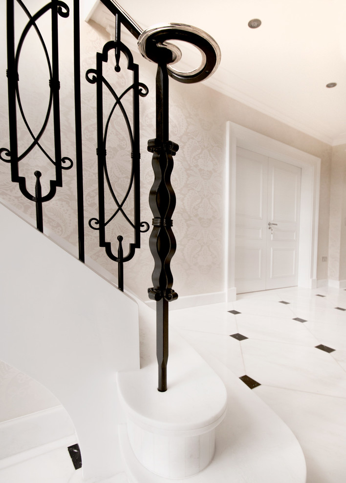 Réalisation d'un grand escalier courbe tradition en marbre avec des contremarches en marbre et un garde-corps en métal.