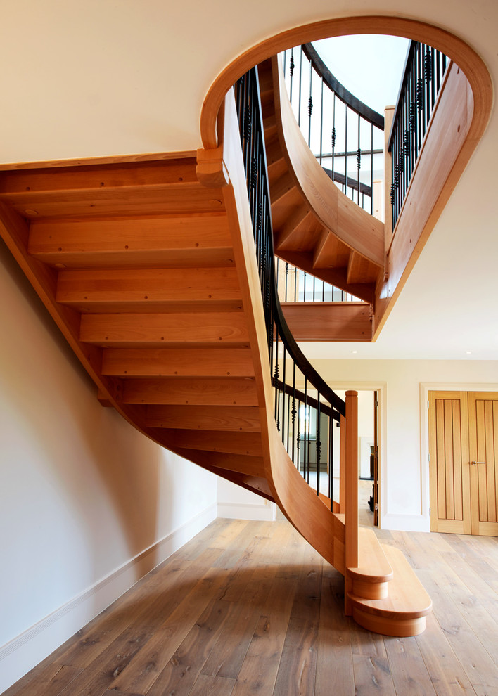 Ejemplo de escalera curva rústica grande con escalones de madera, contrahuellas de madera y barandilla de metal