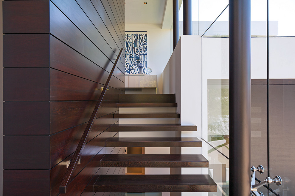 Cette photo montre un grand escalier sans contremarche flottant moderne avec des marches en bois, un garde-corps en verre et du lambris.
