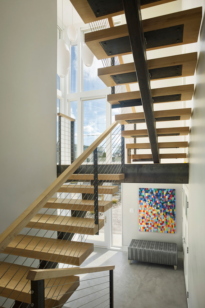 Large trendy wooden floating cable railing staircase photo in Other