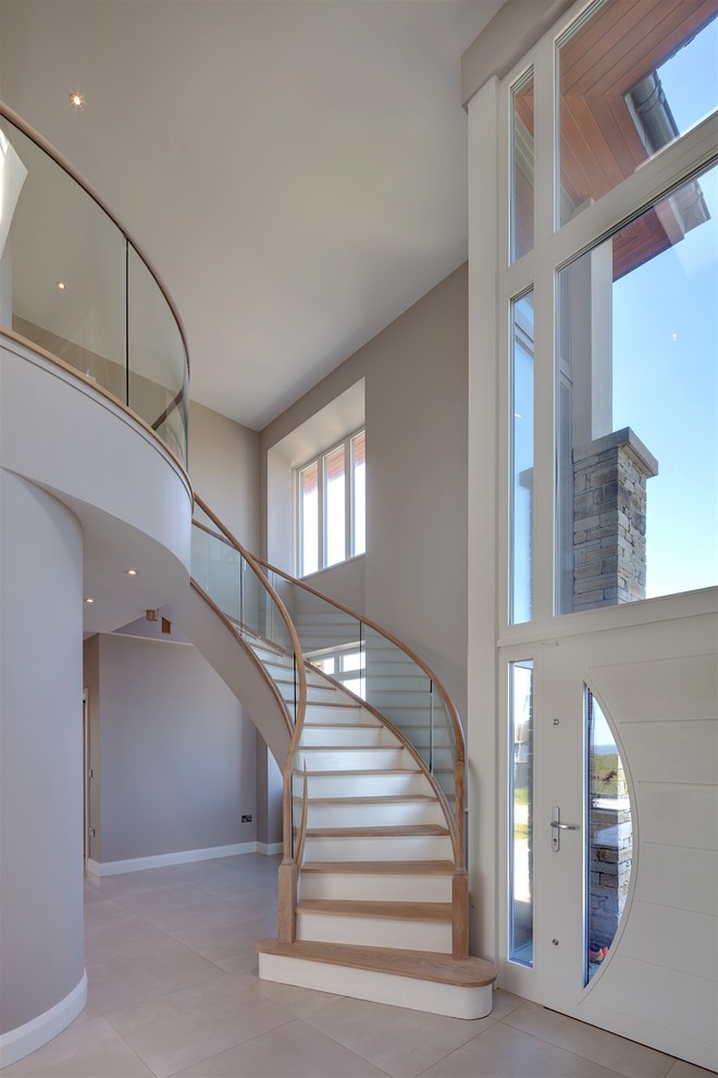 Aménagement d'un grand escalier courbe contemporain avec des marches en bois, des contremarches en béton et un garde-corps en verre.