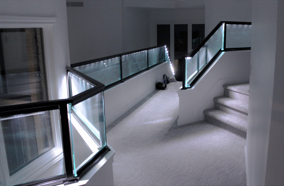 デトロイトにある高級な中くらいなコンテンポラリースタイルのおしゃれなかね折れ階段 (カーペット張りの蹴込み板、ガラスフェンス) の写真