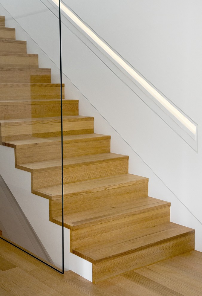Diseño de escalera recta minimalista grande con escalones de madera, contrahuellas de madera y barandilla de vidrio