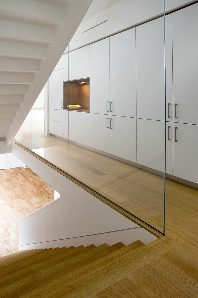Идея дизайна: большая п-образная лестница в стиле модернизм с деревянными ступенями, крашенными деревянными подступенками и стеклянными перилами