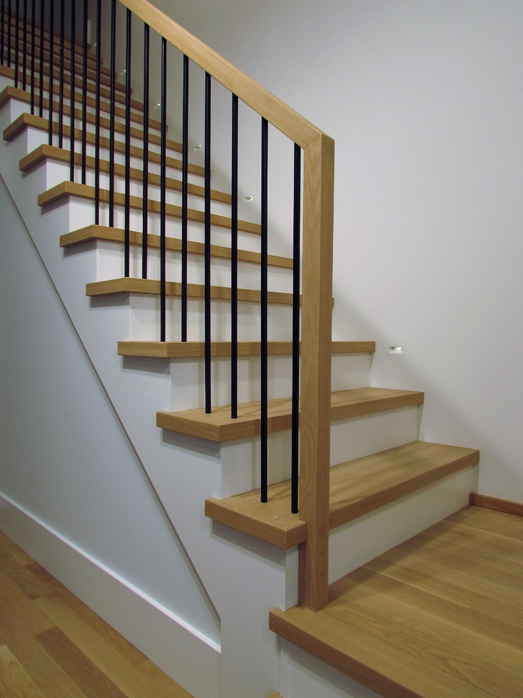 Réalisation d'un grand escalier design en L avec des marches en bois, des contremarches en bois et un garde-corps en métal.