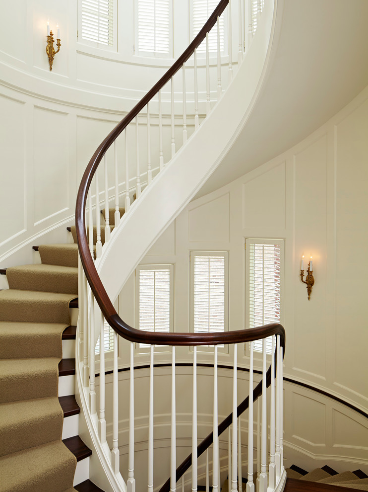 This is an example of an expansive classic wood curved staircase in Chicago with painted wood risers.