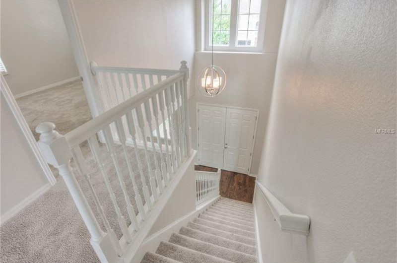 Пример оригинального дизайна: большая прямая лестница в классическом стиле с ступенями с ковровым покрытием, крашенными деревянными подступенками и деревянными перилами
