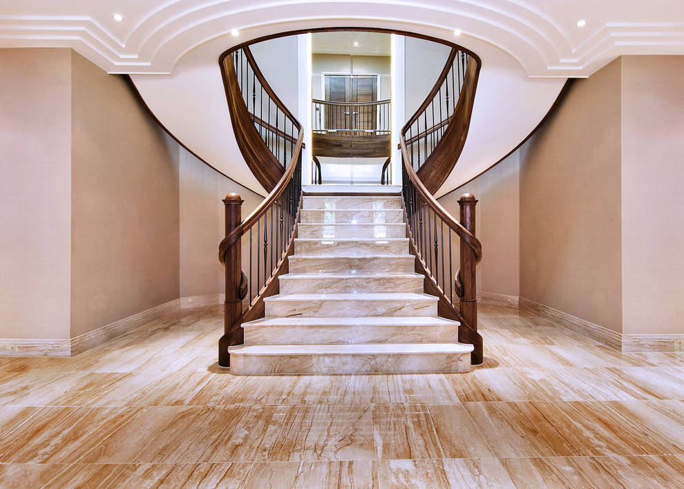 Стильный дизайн: большая изогнутая деревянная лестница в классическом стиле с мраморными ступенями и перилами из смешанных материалов - последний тренд