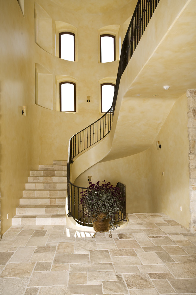 Стильный дизайн: изогнутая лестница в средиземноморском стиле с ступенями из травертина, подступенками из травертина и металлическими перилами - последний тренд