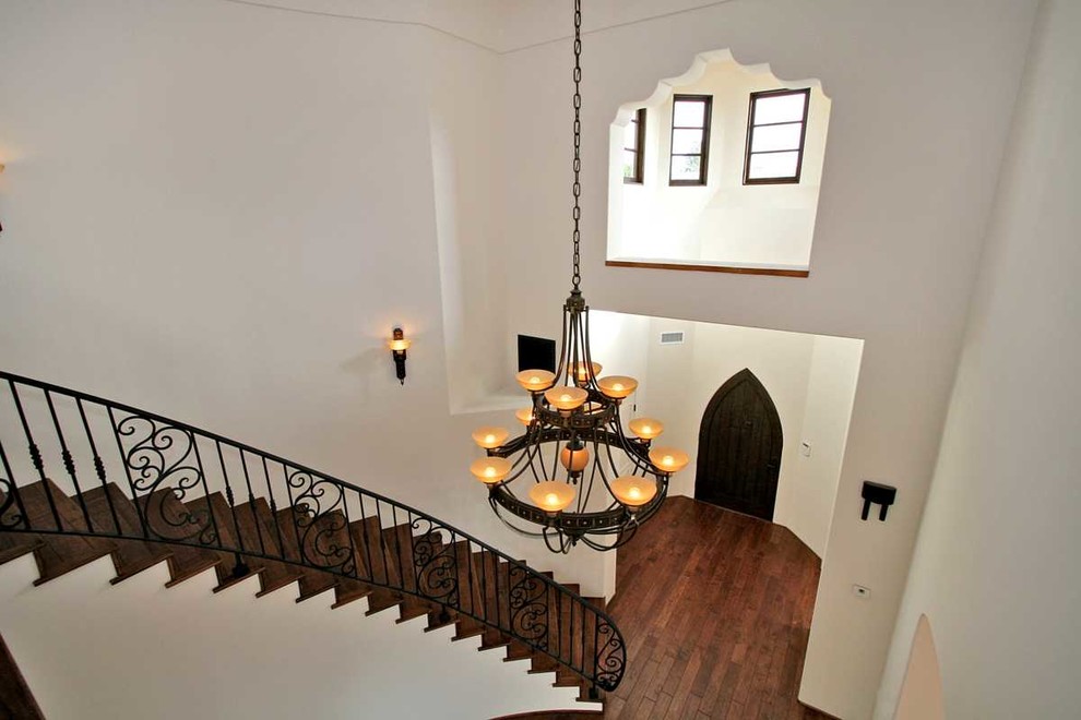 На фото: большая изогнутая лестница в средиземноморском стиле с деревянными ступенями, подступенками из плитки и металлическими перилами с
