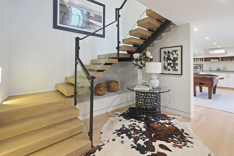 Immagine di una grande scala a "U" minimalista con pedata in legno, nessuna alzata, parapetto in materiali misti e decorazioni per pareti