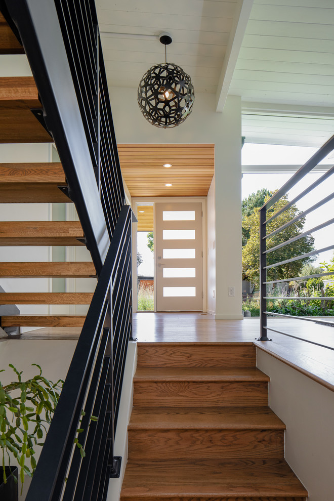 Cette image montre un escalier minimaliste de taille moyenne avec des marches en bois, des contremarches en bois et un garde-corps en métal.