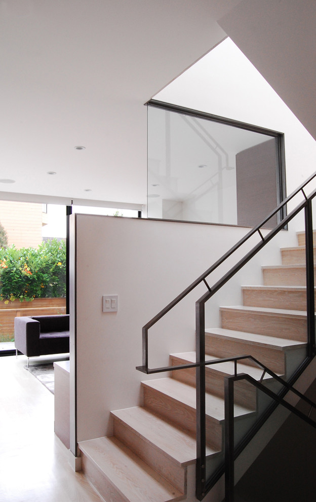 Cette image montre un escalier minimaliste avec des marches en bois, des contremarches en bois et un garde-corps en verre.