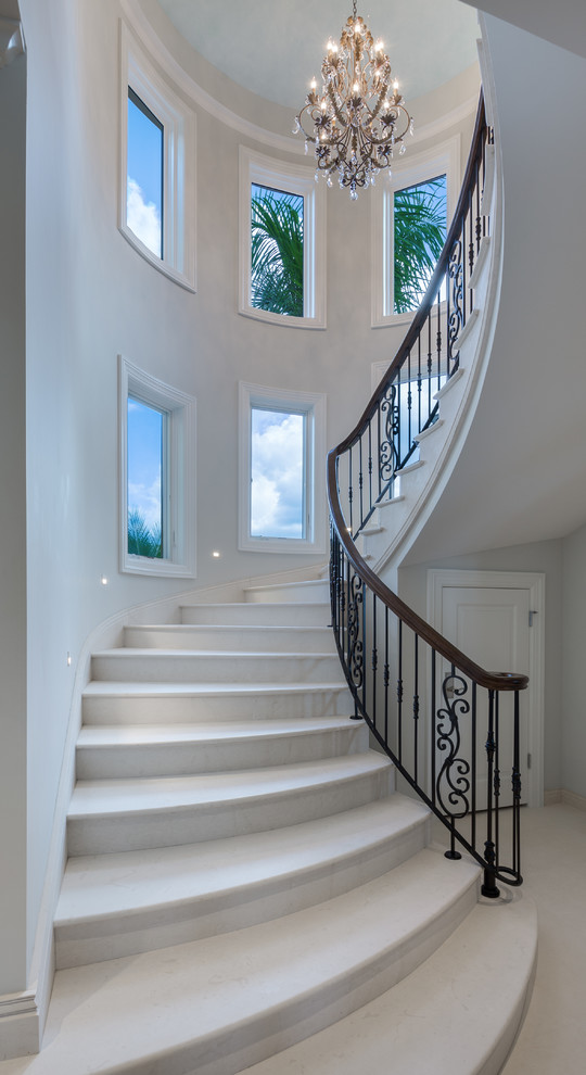 На фото: большая изогнутая лестница в классическом стиле с мраморными ступенями и подступенками из мрамора с