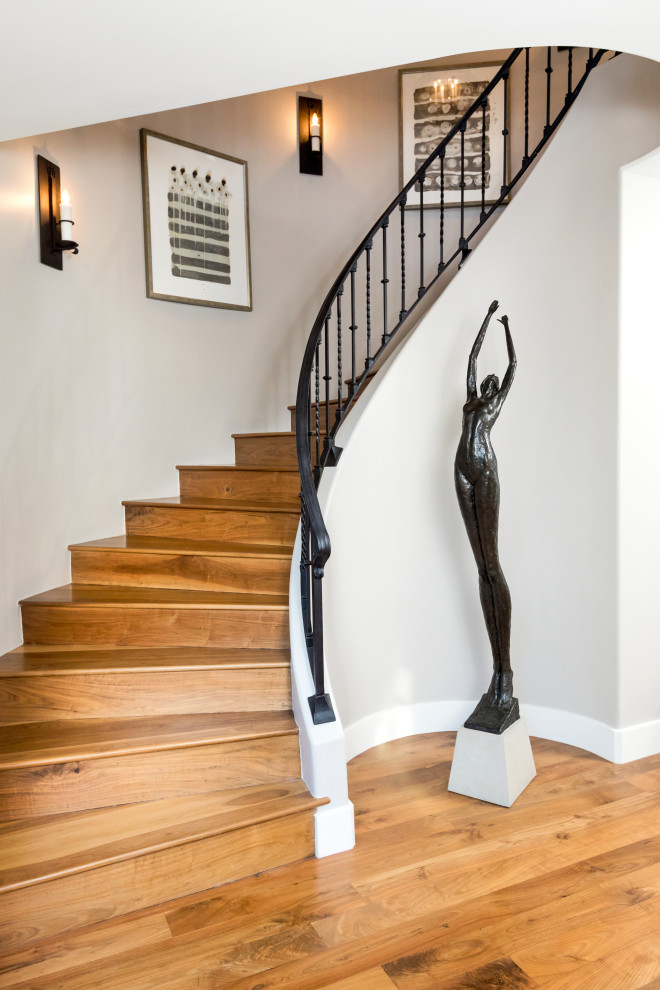 Large mediterranean wood curved metal railing staircase in Los Angeles with wood risers.