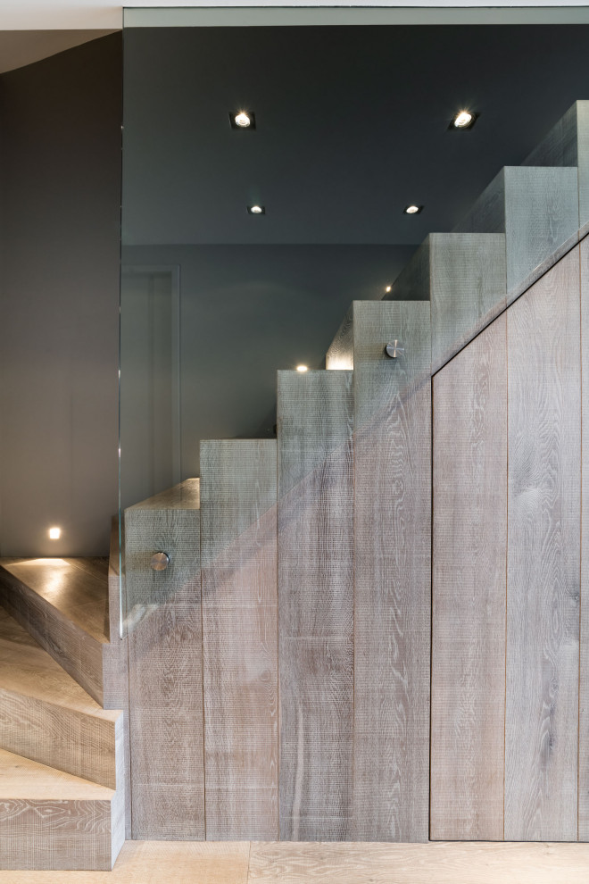 Aménagement d'un très grand escalier courbe contemporain avec des marches en bois, des contremarches en bois et un garde-corps en verre.