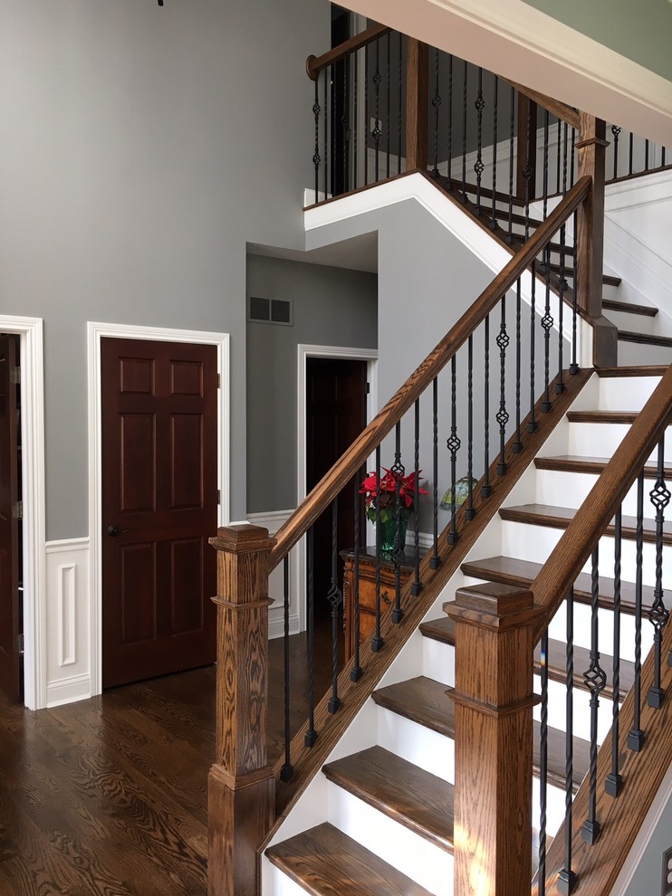 На фото: большая угловая лестница в классическом стиле с деревянными ступенями, крашенными деревянными подступенками и деревянными перилами с