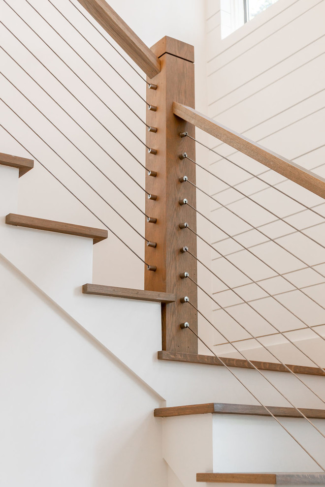 На фото: угловая лестница среднего размера в морском стиле с деревянными ступенями, крашенными деревянными подступенками и перилами из тросов