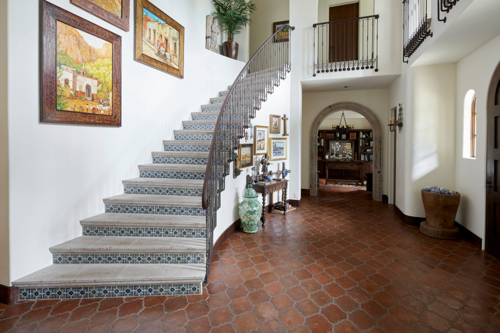 Пример оригинального дизайна: изогнутая лестница в средиземноморском стиле с ступенями из плитки, подступенками из плитки и металлическими перилами