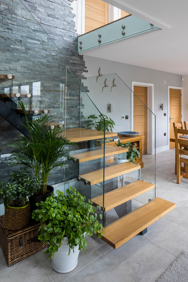 This is an example of a modern wood l-shaped glass railing staircase in London with feature lighting.