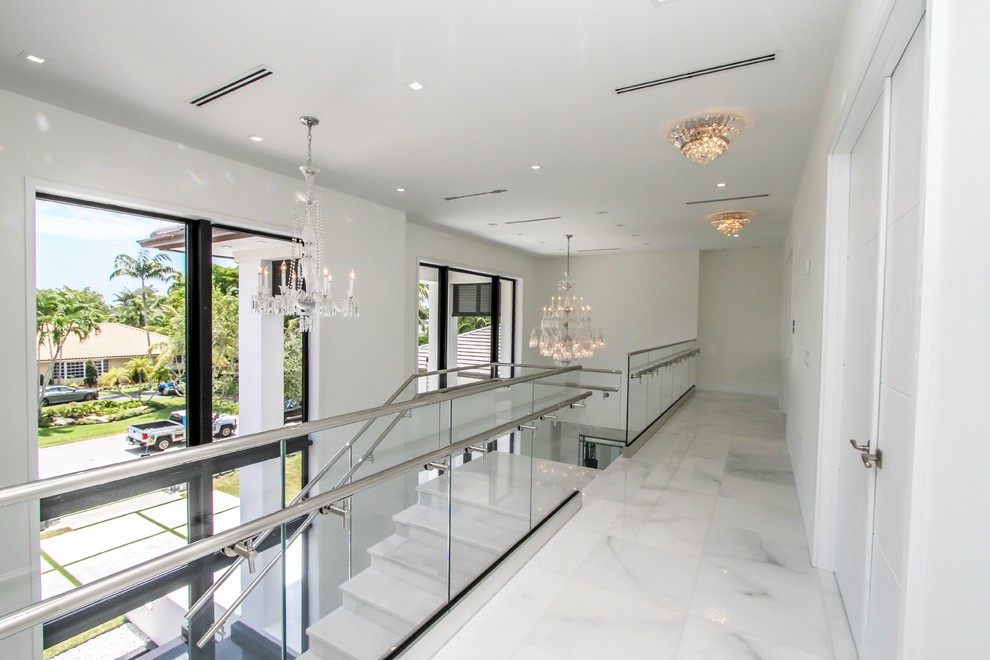 Réalisation d'un grand escalier minimaliste en U et marbre avec des contremarches en marbre, un garde-corps en verre et éclairage.