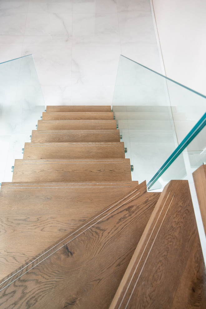 Immagine di una scala a "L" contemporanea di medie dimensioni con pedata in legno, nessuna alzata e parapetto in vetro