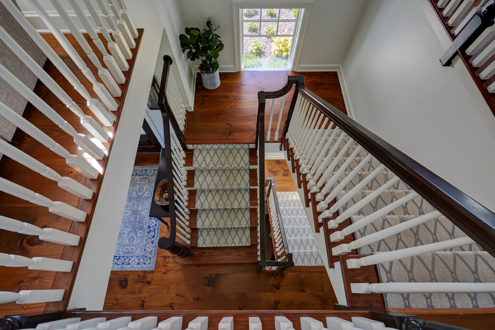 Diseño de escalera en U de estilo de casa de campo extra grande con escalones de madera, contrahuellas de madera pintada y barandilla de madera
