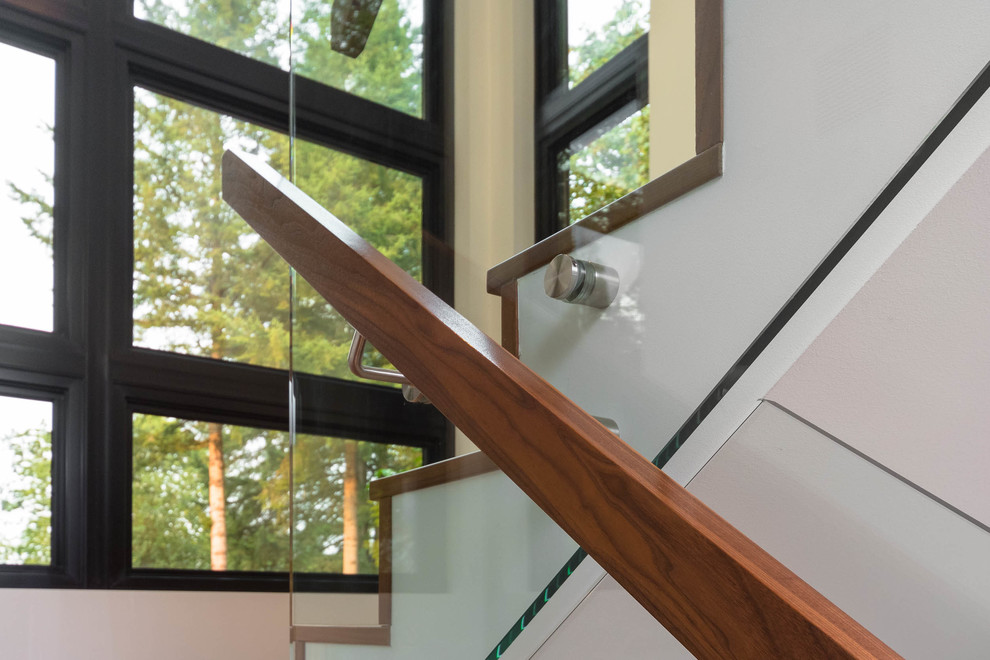 Cette image montre un grand escalier vintage en U avec des marches en bois, des contremarches en bois et un garde-corps en verre.