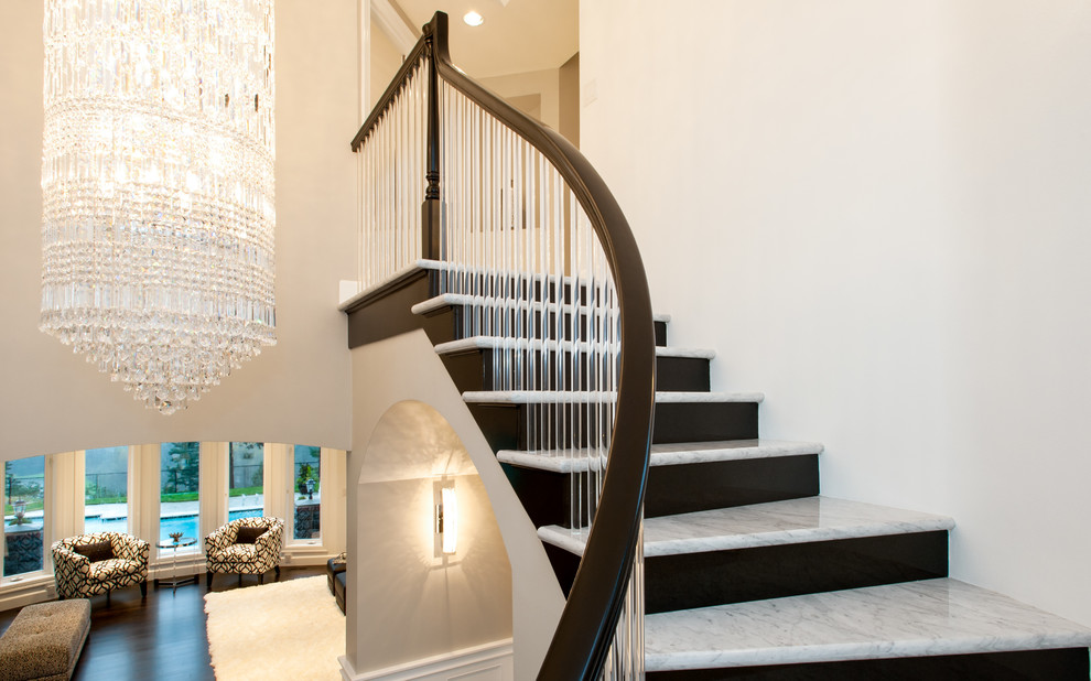 На фото: большая изогнутая лестница в стиле модернизм с крашенными деревянными подступенками и мраморными ступенями с