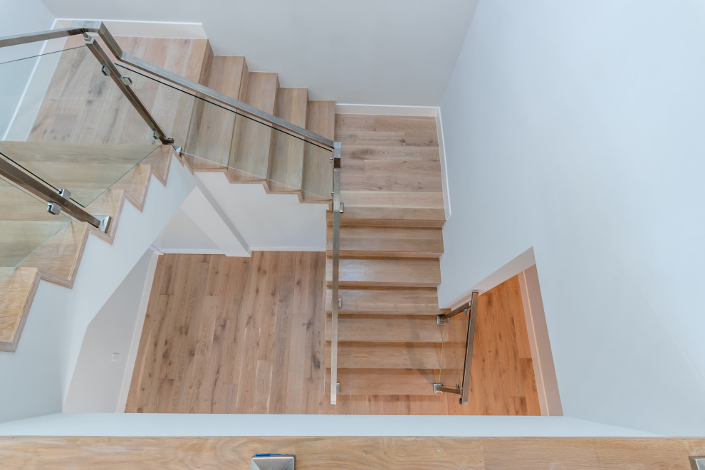 Modelo de escalera en U moderna grande con escalones de madera, contrahuellas de madera y barandilla de vidrio