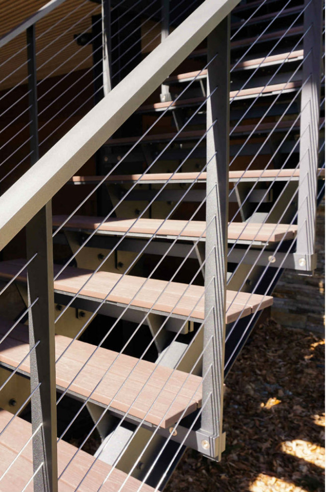 Imagen de escalera suspendida de estilo americano grande sin contrahuella con escalones de metal y barandilla de cable