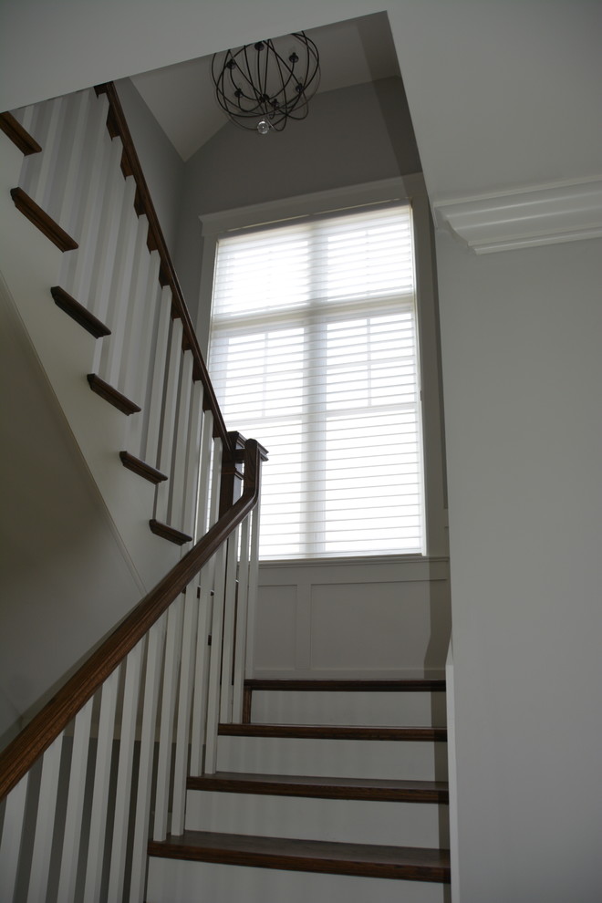Modelo de escalera en U de estilo americano grande con escalones de madera, contrahuellas de madera pintada y barandilla de madera