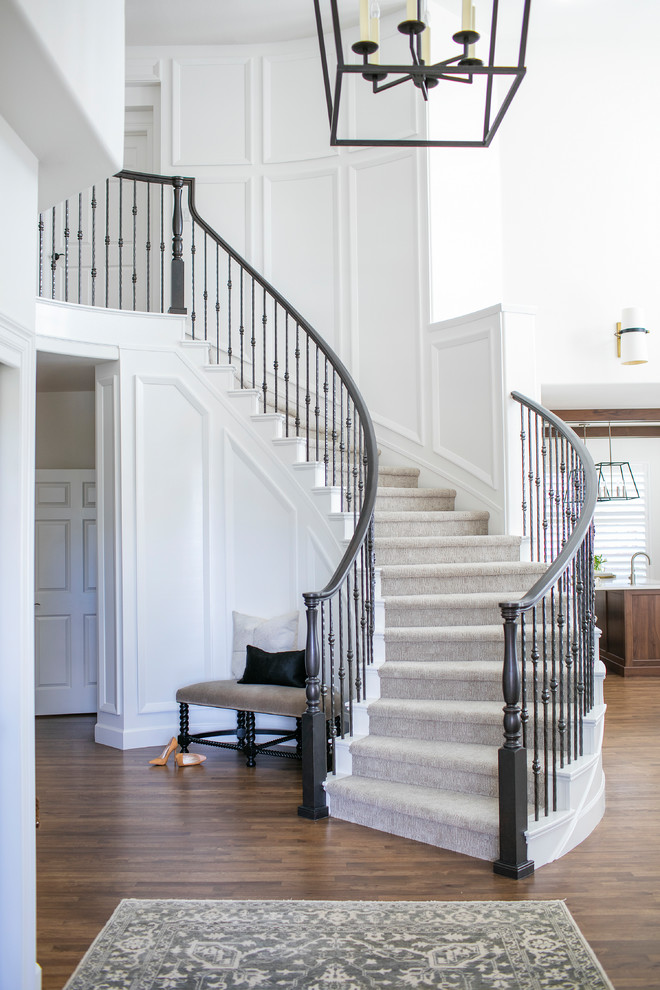 Пример оригинального дизайна: большая изогнутая лестница в стиле неоклассика (современная классика) с крашенными деревянными ступенями, крашенными деревянными подступенками и перилами из смешанных материалов