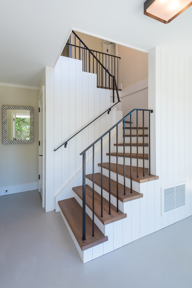 На фото: изогнутая лестница в стиле кантри с деревянными ступенями, крашенными деревянными подступенками и металлическими перилами с