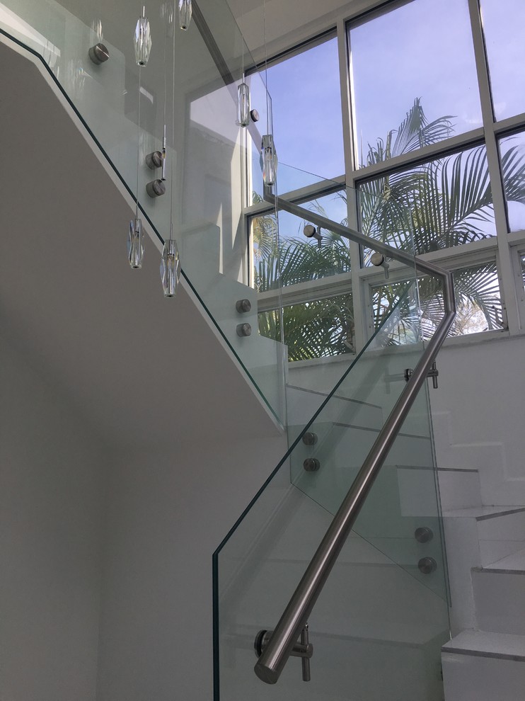 Exemple d'un grand escalier carrelé moderne en L avec un garde-corps en verre et des contremarches carrelées.