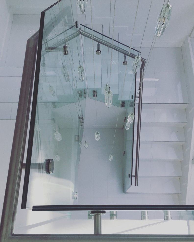 Inspiration pour un grand escalier carrelé minimaliste en L avec des contremarches carrelées et un garde-corps en verre.