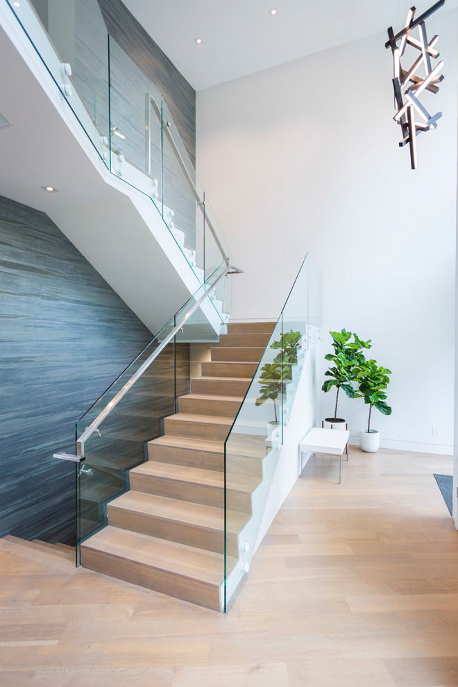 Cette photo montre un grand escalier tendance en L avec des marches en bois, des contremarches en bois et un garde-corps en verre.