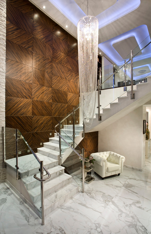 На фото: большая угловая лестница в стиле неоклассика (современная классика) с мраморными ступенями, подступенками из мрамора и стеклянными перилами с