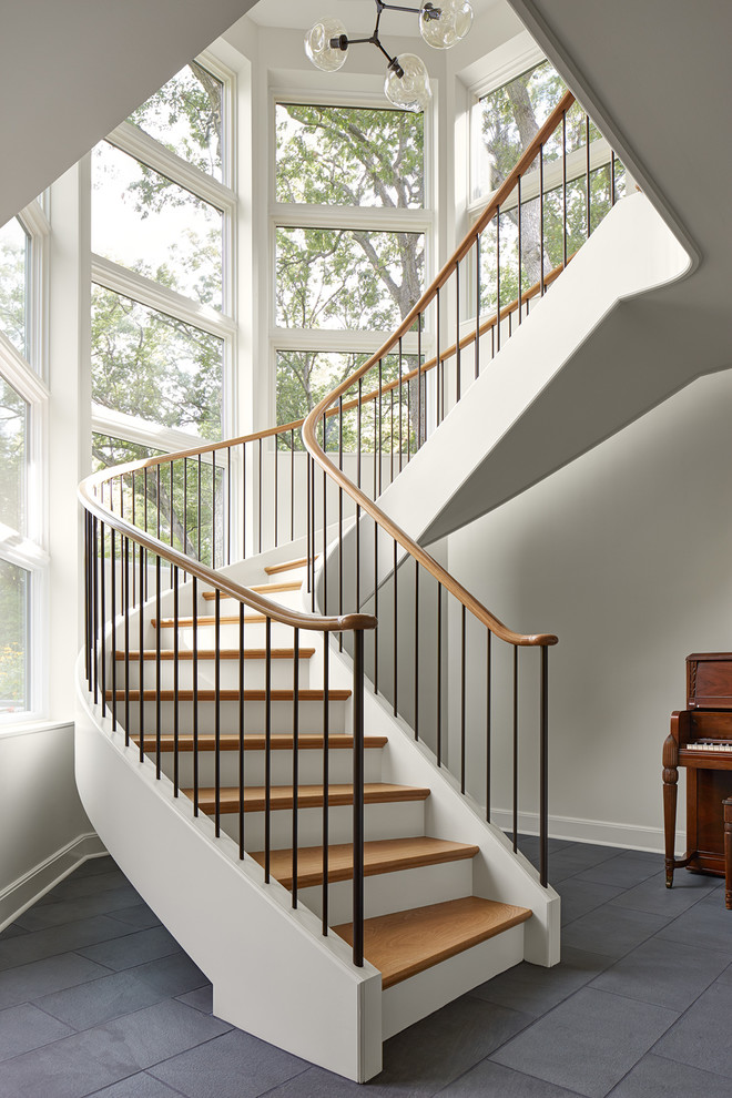 Diseño de escalera curva clásica renovada extra grande con escalones de madera, contrahuellas de madera pintada y barandilla de varios materiales