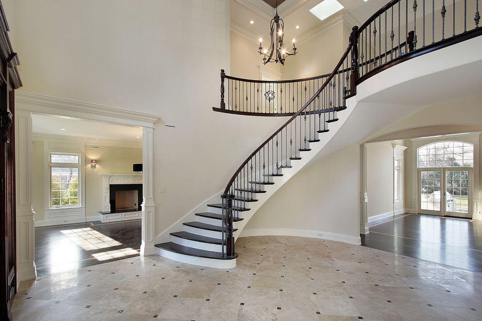 Пример оригинального дизайна: большая изогнутая лестница в викторианском стиле с деревянными ступенями и крашенными деревянными подступенками