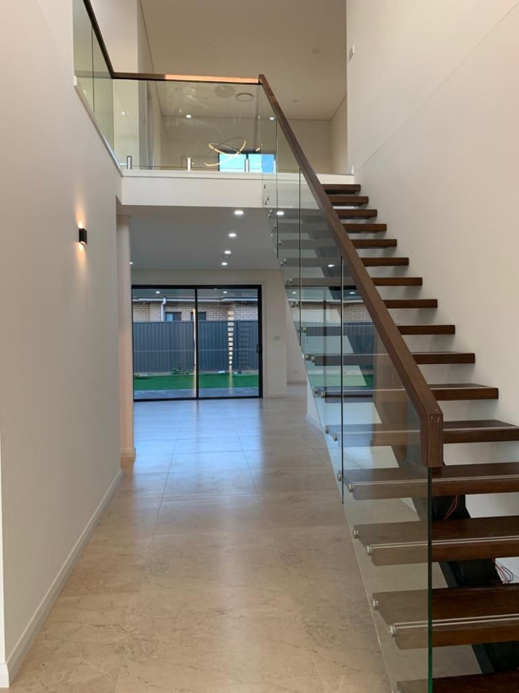 Idée de décoration pour un escalier sans contremarche droit design de taille moyenne avec des marches en bois, un garde-corps en verre et du lambris.
