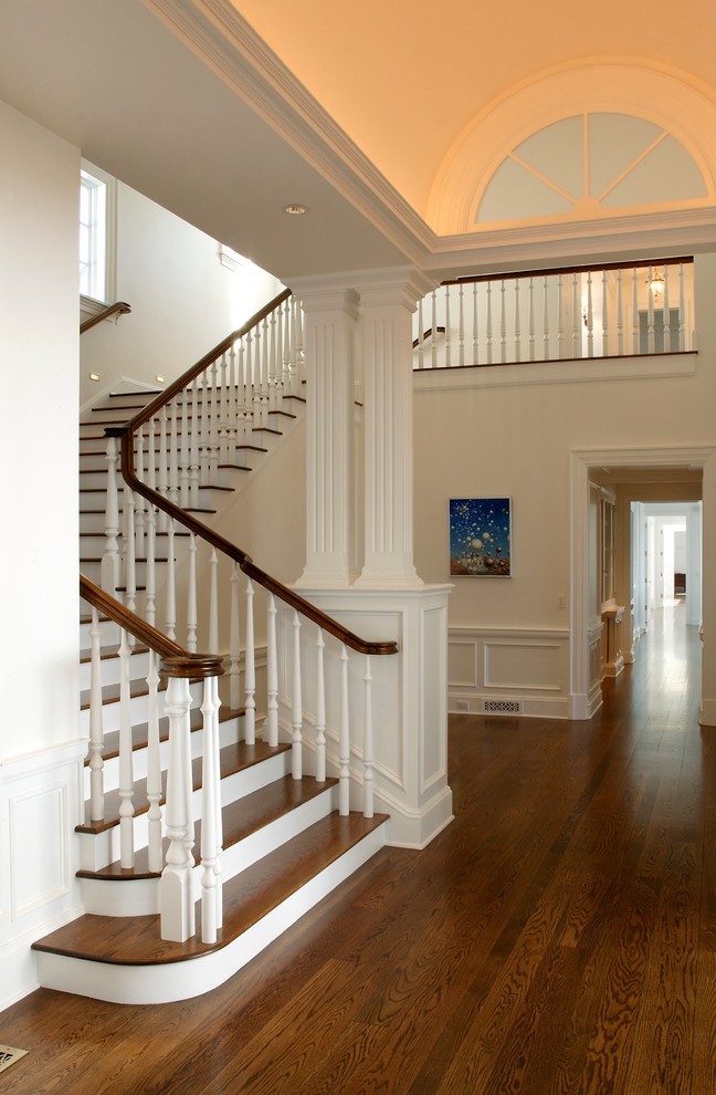 На фото: большая угловая лестница в классическом стиле с деревянными ступенями, крашенными деревянными подступенками и деревянными перилами