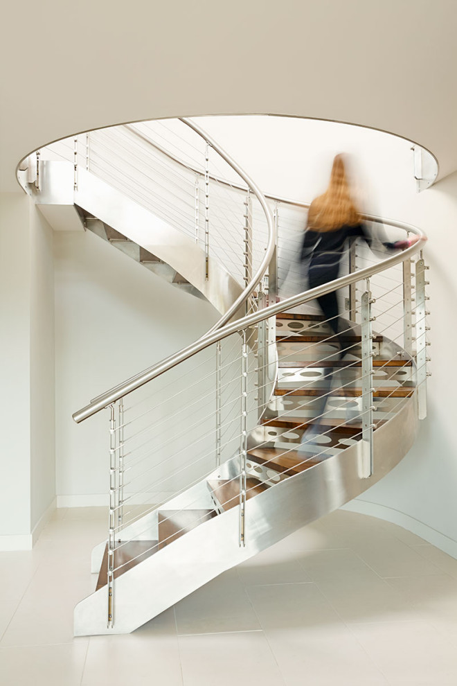 Exemple d'un très grand escalier courbe industriel avec des marches en bois, des contremarches en métal et un garde-corps en câble.