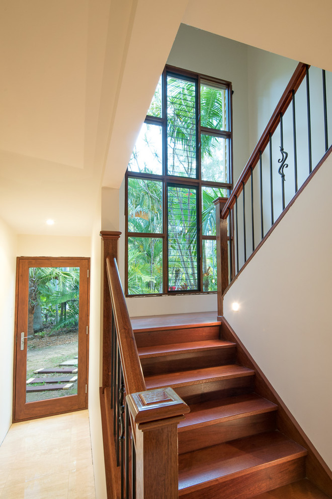 Foto de escalera en U tropical grande con escalones de madera, contrahuellas de madera y barandilla de madera