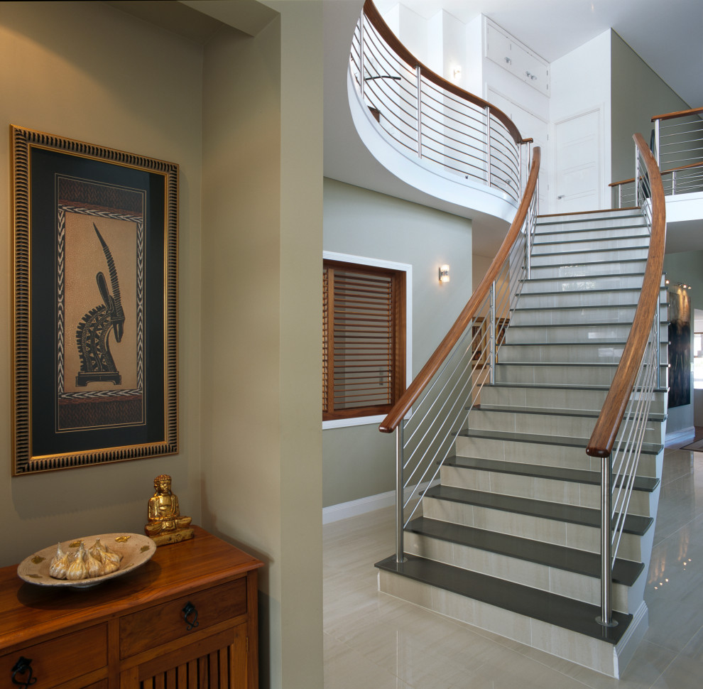 На фото: большая изогнутая лестница в стиле модернизм с ступенями из плитки, подступенками из плитки и перилами из смешанных материалов