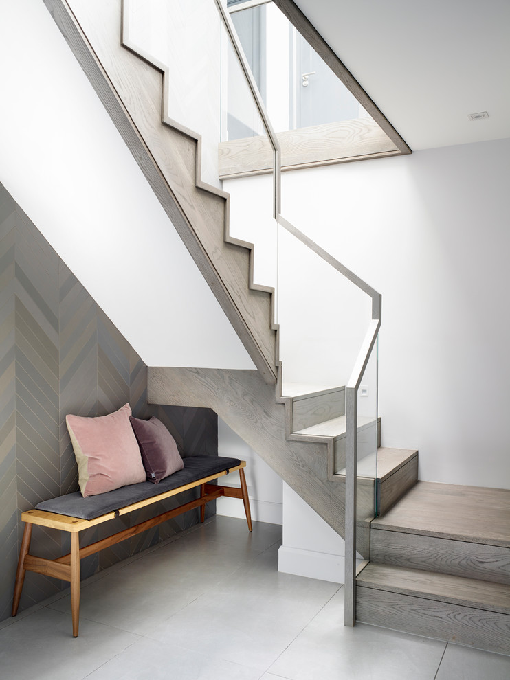 Cette photo montre un grand escalier courbe tendance avec des marches en bois, des contremarches en verre et un garde-corps en métal.