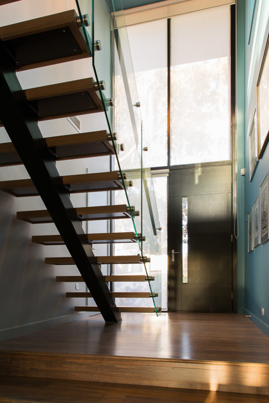 Immagine di una scala a rampa dritta minimal di medie dimensioni con pedata in legno, alzata in vetro e parapetto in vetro
