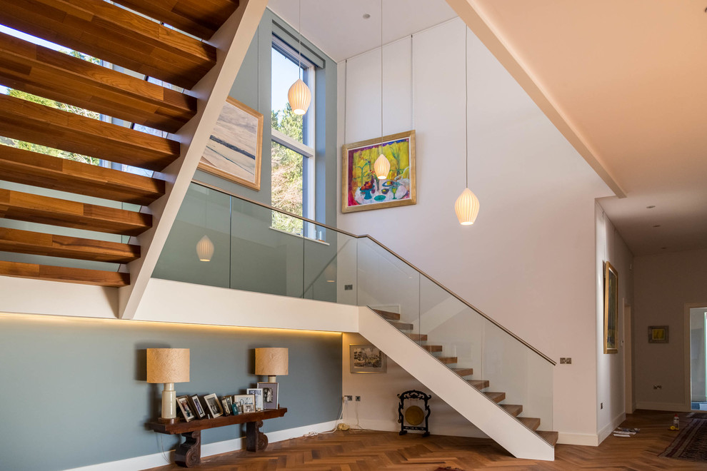 Свежая идея для дизайна: изогнутая лестница с деревянными ступенями, стеклянными подступенками и металлическими перилами - отличное фото интерьера