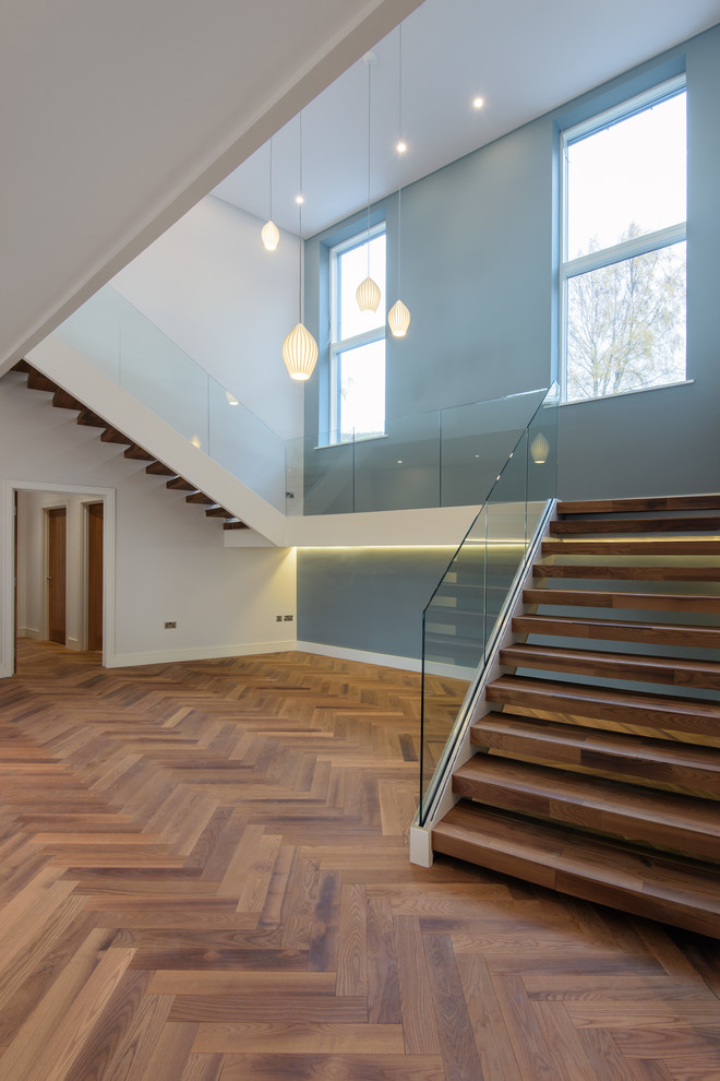 Photo of a large modern wood floating glass railing staircase in Other with open risers.